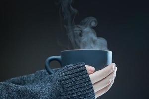 Female hands with a hot Cup of tea on a dark background. Steam rises from the hot drink. photo
