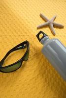 concepto de verano, fondo amarillo vibrante con gafas de sol, botella de agua y estrellas de mar foto