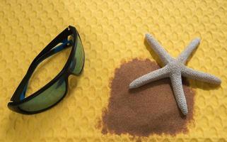 concepto de verano, gafas de sol, estrellas de mar y arena de playa sobre un fondo amarillo vibrante