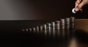 stacks of coins on a black background with a hand putting a coin on the pile photo