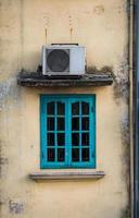 vieja ventana verde con compresor de aire en la pared amarilla foto