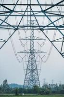 fila de poste de alto voltaje, gran torre eléctrica de transmisión con cable en campo de arroz con cielo azul en el campo foto