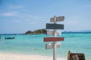 Wooden arrows signpost on white beach with tropical sea photo