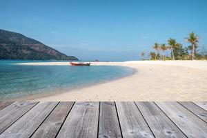 Wooden tabletop on white sand beach with wooden long-tail boat in tropical sea photo