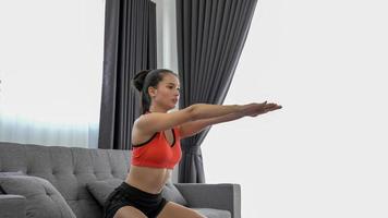 Young muscular fitness woman doing half squats exercise at home on living room ,sofa workout photo