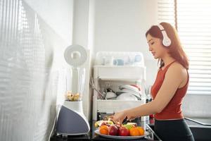 The sportswoman making smoothies from fruits in the kitchen at home while listening to music through headphones - lifestyles concepts photo