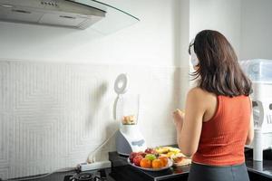 la deportista haciendo batidos de frutas en la cocina de casa mientras escucha música a través de auriculares - conceptos de estilo de vida foto