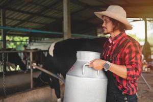 granjero que lleva un barril de leche pasa por el establo de vacas lecheras, granja de vacas, pequeña empresa foto