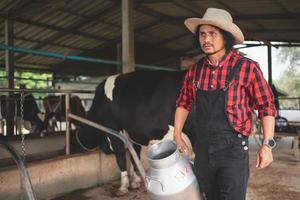 granjero que lleva un barril de leche pasa por el establo de vacas lecheras, granja de vacas, pequeña empresa foto