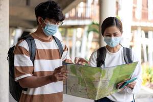 Travel, man and woman are reading paper map. wearing mask, carry backpacks. stripped shirt and eyeglasses photo