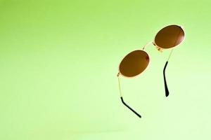 Flying brown golden sunglasses on green background. photo