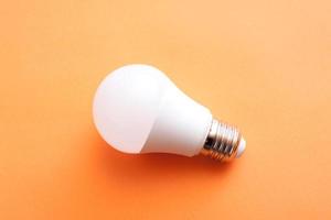 White economy light bulb on orange background. photo