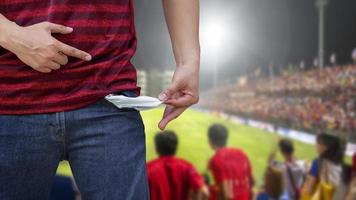 Man showing his empty pockets on blurred soccer stadium. photo