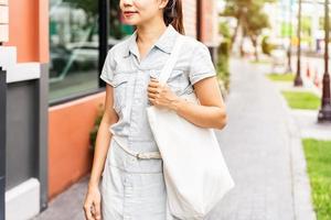 Young asian woman holding a reusable bag and walking in the city, Zero waste concept photo