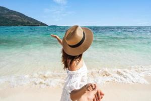 joven pareja viajera tomándose de la mano relajándose y disfrutando en la hermosa playa tropical de arena blanca con espuma de olas y mar transparente, vacaciones de verano y concepto de viaje foto