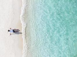 Young man sitting and relaxing at beautiful tropical white sand beach with wave foam and transparent sea, Summer vacation and Travel background Top view from drone photo