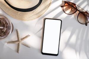 teléfono inteligente de pantalla vacía con accesorios de viaje en la mesa, concepto de vacaciones de verano foto