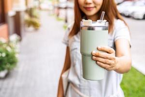 Young asian woman holding a reusable tumbler glass and walking in the city, Zero waste concept photo