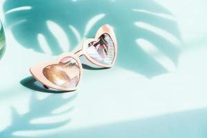 Sunglasses with a view of the beach reflecting in front of the lens against a backdrop of shadow of tropical leaves photo