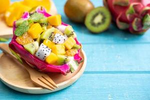 Mix tropical fruits salad served in half a dragon fruit on wooden table photo