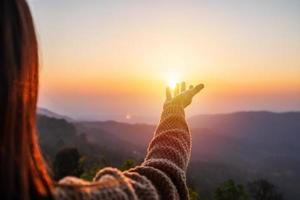 mano de mujer joven alcanzando las montañas durante la puesta de sol y el hermoso paisaje foto