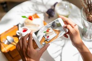 Young woman taking photo of dessert with smart phone for social media in restaurant while traveling