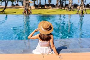 Young woman traveler relaxing and enjoying by a tropical resort pool while traveling for summer vacation photo
