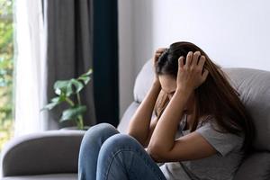 mujer asiática joven solitaria que se siente deprimida y estresada en la sala de estar en casa, concepto de emoción negativa foto