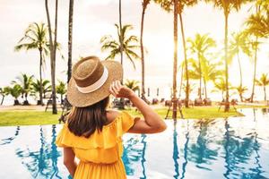 Young woman traveler relaxing and enjoying the sunset by a tropical resort pool while traveling for summer vacation photo
