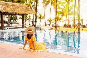 Young woman traveler relaxing and enjoying the sunset by a tropical resort pool while traveling for summer vacation photo