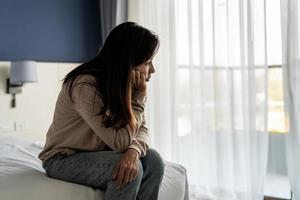 joven solitaria que se siente deprimida y estresada sentada en el dormitorio oscuro, emoción negativa y concepto de salud mental foto