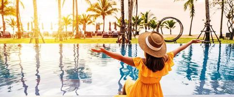 joven viajera relajándose y disfrutando de la puesta de sol junto a una piscina tropical mientras viaja de vacaciones de verano foto