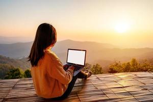 joven viajera independiente que trabaja en línea usando una computadora portátil y disfrutando del hermoso paisaje natural con vista a la montaña al amanecer foto