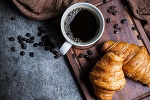 desayuno con cruasanes recién hechos y una taza de café negro sobre tabla de madera foto