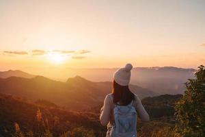 Happy young woman traveler relaxing and looking at the beautiful sunset on the top of mountain photo