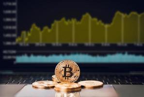 un bitcoin dorado se coloca en el teclado frente a una pantalla de velas o gráficos del mercado de acciones o criptomonedas con una computadora portátil, comercio de criptomonedas y concepto de inversión foto