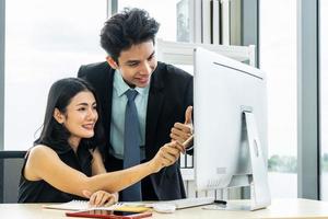 ya tenemos excelentes resultados, una joven empresaria señalando una computadora portátil con una sonrisa y discutiendo algo con su compañero de trabajo y él lo aprueba mientras trabaja en la oficina foto