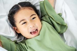 adorable niña asiática feliz después de dormir en su cama blanca divertido niño feliz jugando y sonriendo. foto