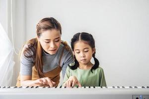 Happy little Asian deaughter playing piano with mother at home, Mother teaching daughter to play piano,They play and sing songs. They are having fun. photo