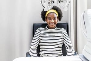 Smiling young woman african american afro hair after doing eyesight measurement with optical phoropter photo