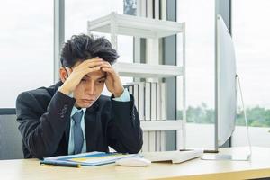 hombre de negocios asiático deprimido por trabajar en la computadora portátil en la oficina foto
