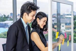 Asian creative business women and man are writing note on the text sheet after thinking new idea and planning project with colleague ,Group of employee brainstorming idea on glass wall and sticky photo