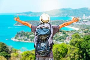 retrato de vista trasera de un joven viajero con mochila de pie en una montaña con los brazos abiertos, estilo de vida de viaje y concepto de aventura. foto