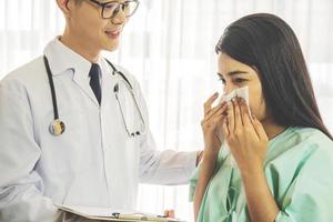 Primary care doctor making diagnosis to sick woman, unhappy patient using a tissue to sneeze and blowing her nose and get high fever from flu and cold, Patient care and healthcare. photo