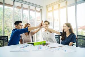 equipo de empresarios asiáticos con traje informal de pie y dando cinco en la oficina, acción feliz para el trabajo en equipo en el lugar de trabajo moderno, el grupo de empleados celebra juntos el éxito corporativo foto