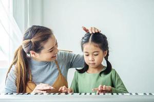 Happy little Asian deaughter playing piano with mother at home, Mother teaching daughter to play piano,They play and sing songs. They are having fun. photo