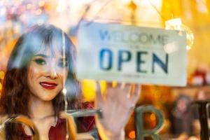 Smiling asian young woman setting open sign broad at the shop glasses for welcome the customer in to the coffee shop, small business owner and startup with cafe shop, ready to service photo