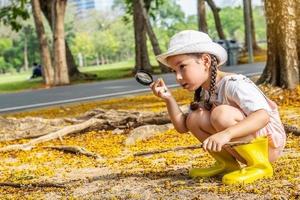 Image of cute girl exploring the nature with magnifying glass outdoors, Child playing in the forest with magnifying glass. Curious kid searching with magnifier on the grass in the park photo