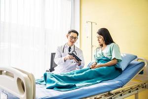 Asian male doctor talking to asian female patient in bed, while explaining exam results in computer to patient at medical consultation, Medicine and health care concept, selective focus point photo