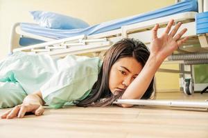 Female asian patient fell lying on the floor at hospital. She is trying to raise their hand and ask for help, There was a support rod falling to the wooden floor, accident or other health photo